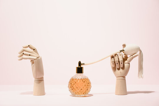 Stylish transparent bottle of perfume placed between wooden hands placed on pink background in light studio