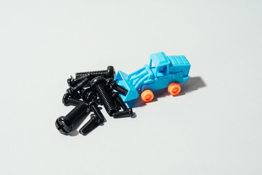 From above of small plastic toy tractor collecting various black screws on white table