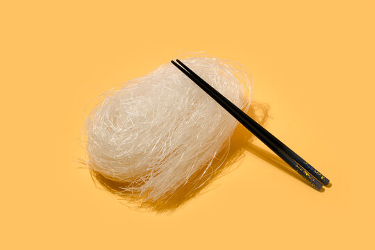 Portion of rice noodles with black chopstick placed on light surface against yellow background in studio