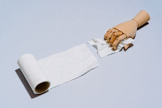 Composition of wooden hands unwinding roll of white toilet paper against blue background
