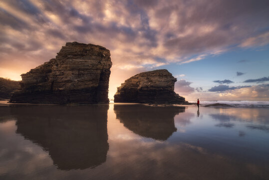 Silhouette of anonymous person standing on wet As Catedrais beach with rocks under sundown sky in Galicia