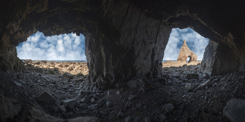 Rough cave scenery of sharp severe rock with hole on stony Campiecho Beach under blue sky in Asturias