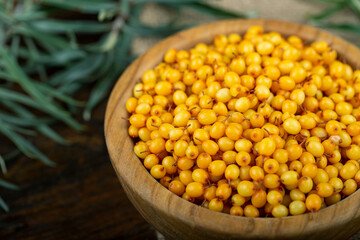 Sea buckthorn. Fresh ripe berry in wooden bowl with leaves on wood background.