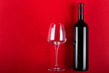 Red wine bottle and empty wine glass. on a red background. Romantic mood. Space for text.