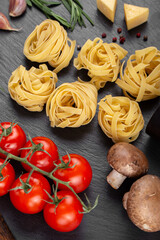 Raw pasta tagliatelle with fresh tomatoes, peppers, mushrooms,asparagus beans, spices and cheese on black table.