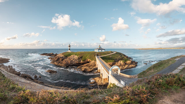 Spectacular scenery of bridge leading to rocky island covered with green grass with lighthouse placed in wavy ocean in Faro Illa Pancha in Galicia in Spain in daytime