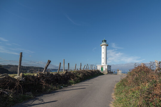 Asphalt road leading to white lighthouse placed in Faro de Lastres in Asturias in Spain under cloudless blue sky in daytime