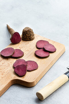 From above composition of ripe raw beetroot slices placed on wooden cutting board on kitchen table near sharp knife