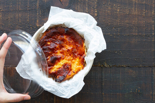 From above cropped unrecognizable peron with delicious baked cheesecake served on a container in a wooden table