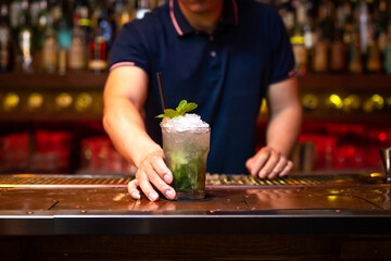 Hand of unrecognizable bartender gives you a well elaborated mojito cocktail in the bar after he finished to prepare it