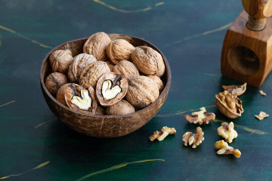 Round shaped wooden bowl full of crunchy walnuts with dry uneven nutshells on table