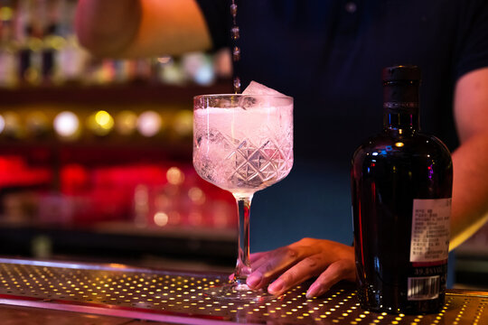 Young Asian bartender pouring tonic water to the glass for preparing a gin tonic cocktail in the bar