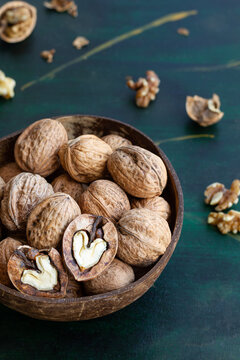 Round shaped wooden bowl full of crunchy walnuts with dry uneven nutshells on table