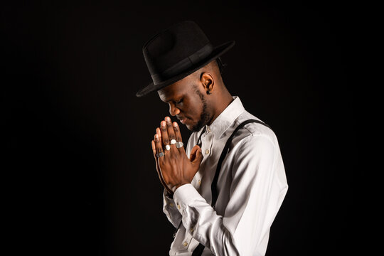 Side view of young unshaven African American male in white shirt and rings on fingers with prayer hands