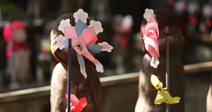 A slow motion of moving colorful windmills with Jizo statue daytime closeup