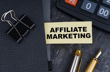 On the table is a calculator, a pen and a notebook with a bookmark on which it is written - Affiliate Marketing