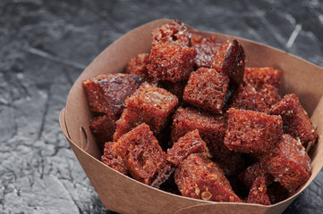 dark croutons in a craft container on an isolated dark background. Take away food. Photo for menu and site. Close up. High quality photo