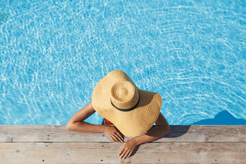 Enjoying summer vacation. Stylish woman in hat relaxing in pool water at wooden pier, top view....