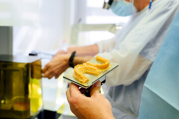 Side view of crop unrecognizable male dentist in uniform near colleague with jaw casts and medical milling machine in hospital