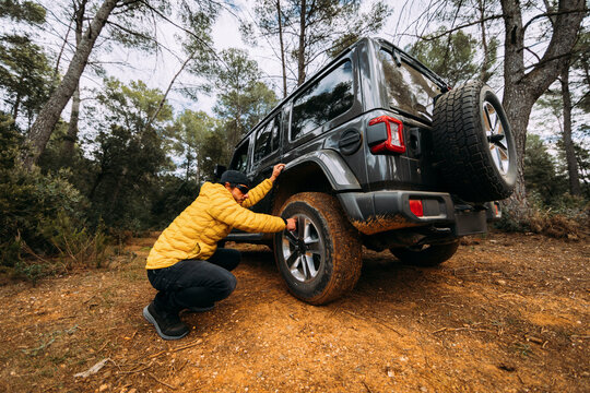 Side view of an adventurer checking the pressure of the wheels of his off-road car in the mountains