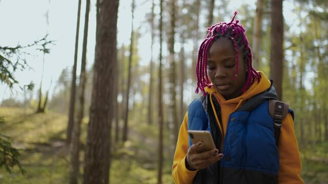 black woman with Backpack Using Smartphone Gps. African american girl Hiking In The Forest And Typing Message On Smartphone. Solo female hiker using smart phone of forest.