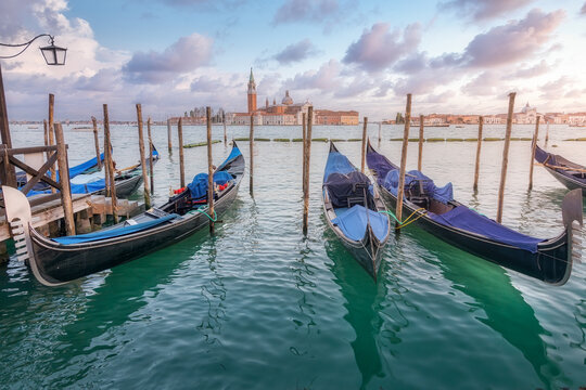 Traditional gondolas moored on rippling water surface on background of city and sundown sky in Venice