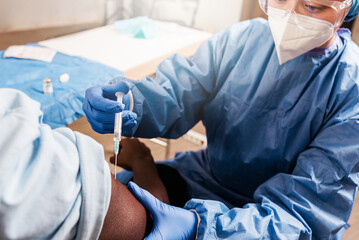 Cropped female doctor in protective uniform and latex gloves vaccinating unrecognizable male African American patient in clinic during coronavirus outbreak