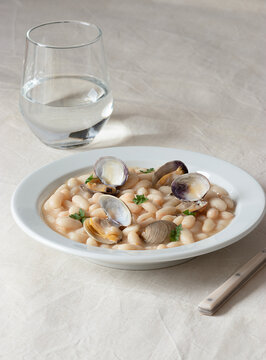 Appetizing traditional spanish stewed white fabes beans with mollusks in plate with fresh parsley leaves on tablecloth