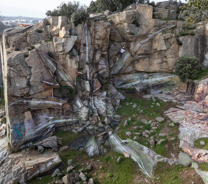 Drone view of man in helmet hanging on rope while painting graffiti on steep stony slope
