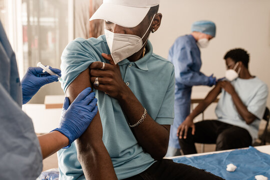 Cropped doctor in protective uniform and latex gloves vaccinating unrecognizable male African American patient in clinic during coronavirus outbreak