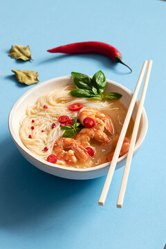 Tom yum soup in bowl with chopsticks on blue background