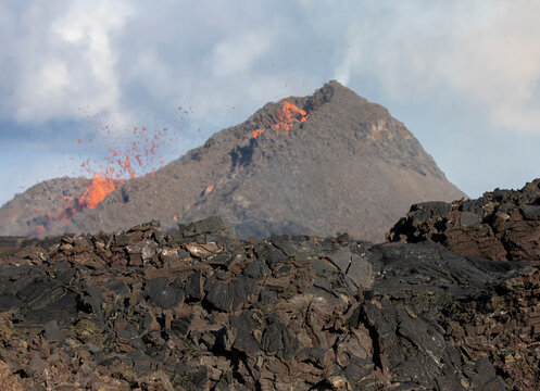 Side view of magma sparks out of the volcano hole and run like rivers of lava over the ground in Iceland