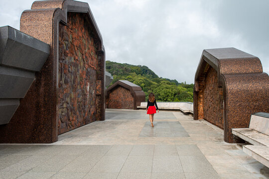 Back view of faceless female tourist strolling on tiled walkway between monuments against green mount in Thailand