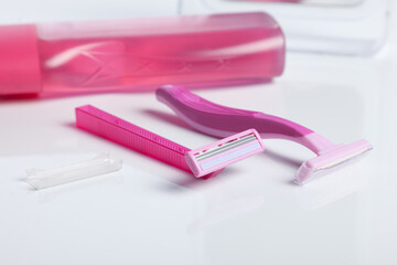 Two pink razor on white table front of a shower gel.