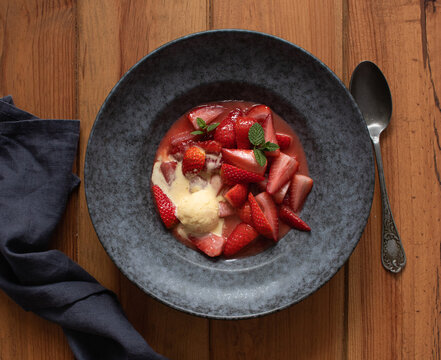 Top view of tasty flambeed strawberry halves with vanilla ice cream in plate on wooden table