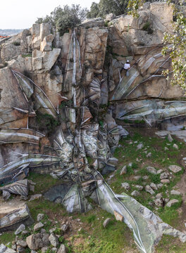 Drone view of man in helmet hanging on rope while painting graffiti on steep stony slope