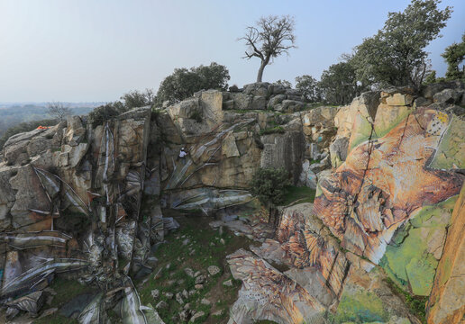 Drone view of man in helmet hanging on rope while painting graffiti on steep stony slope