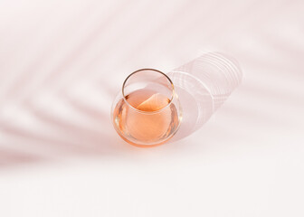 Glass with a strong drink, its shade and the shade of a palm tree on a white background.