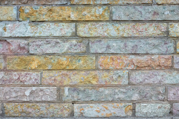Fragment of the wall of the building, faced with early-colored decorative stone. The surface has a nice texture. There are cement joints. Background.