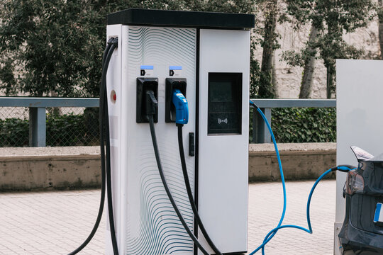 Modern alternative energy electric car connected to charging station with plug of power cable supply on urban street