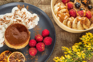 From above of tasty flan with whipped cream and fresh raspberries near bowl full of banana slices and berries with caramel sauce