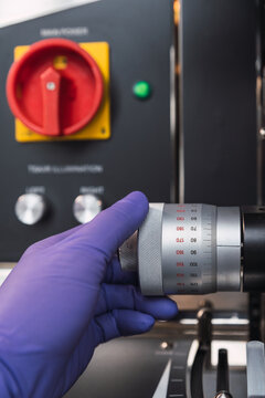 Crop faceless laboratory specialist in latex gloves adjusting powerful microscope knob while working in modern lab
