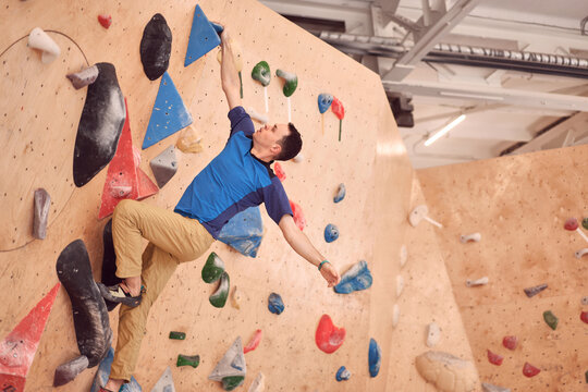 Low angle of muscular male alpinist hanging on climbing wall while training in bouldering center