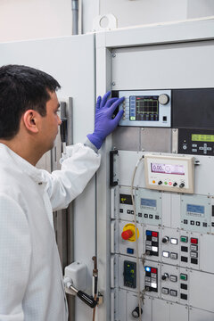 Crop concentrated professional male laboratory assistant in white robe and latex gloves pressing buttons on modern equipment