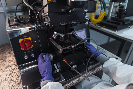 Cropped unrecognizable expert person in lab coat gloves examining samples through powerful microscope lenses while working in modern equipped laboratory