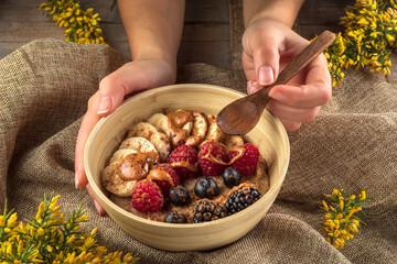 Crop anonymous cook showing bowl with banana slices and assorted fresh berries with caramel sauce for breakfast
