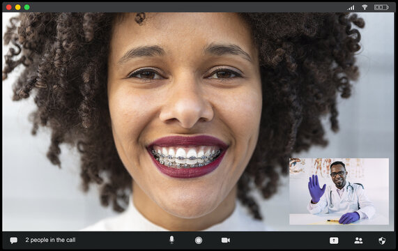 Crop cheerful African American female patient with braces smiling at camera while talking with male doctor waving hand during video chat