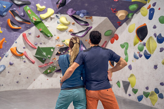Back view of unrecognizable couple of alpinists embracing in modern climbing center with artificial wall