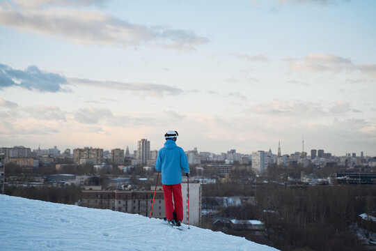 Back view anonymous male skier in warm sportswear skiing along snowy hill slope in winter city park