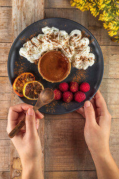From above of crop anonymous cook with plate of yummy baked flan with ripe raspberries and cinnamon powder